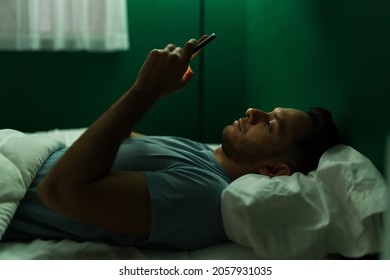 Handsome latin man texting on his smartphone and checking social media before falling asleep at night