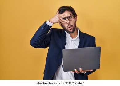 Handsome Latin Man Working Using Computer Laptop Peeking In Shock Covering Face And Eyes With Hand, Looking Through Fingers With Embarrassed Expression. 