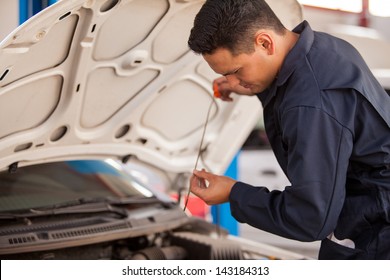 Handsome Latin mechanic measuring the oil level of an engine at an auto shop