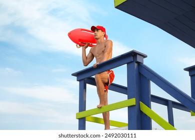 Handsome lifeguard with life buoy on watch tower against sky - Powered by Shutterstock