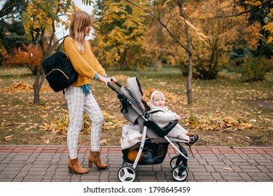 Handsome Little Baby With Big Blue Eyes, Short Red Hair, Pump Lips In A Stroller Outside In The Fall With Its Nice Happy Mum