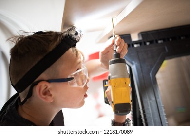 A Handsome Little Boy With ADHD, Autism, Aspergers Syndrome, Using A Drill With A Head Torch And Safety Eye Glasses On For Protection, DIY Homework Project For School