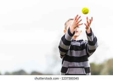 A handsome little boy with ADHD, Autism, Aspergers Syndrome practices his catching coordination with a tennis ball at the park, tennis coaching