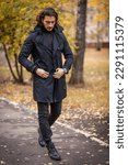 Handsome long haired man in black trench coat walking in the park in wonderful autumn day. Fashion and style concept