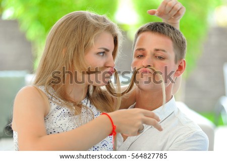 Handsome long haired young blonde woman sitting on a couch, hugging her husband and fooling around