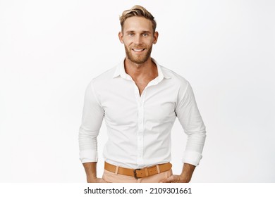 Handsome macho man with blond hair and beard, smiling and looking confident at camera, wearing white shirt, standing against studio background - Powered by Shutterstock