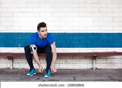 Handsome Male Athlete Sitting And Tying Shoelaces On The Bench