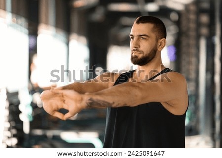 Handsome male athlete stretching arms before workout at gym, making hands in lock exercise, young muscular man bodybuilder performing wrist stretch, demonstrating post-exercise cooldown routine