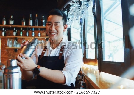 Handsome male bartender in apron preparing drink for customer at bar counter. Asian bartender man making some drink for guest of hotel.