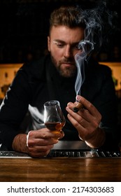 Handsome Male Bartender Holding In His Hands A Glass Of Strong Alcoholic Drink And Smoking Cuban Cigar