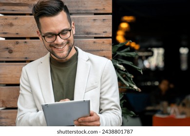 Handsome male business person standing outdoors in front of a local coffee shop and checking financial reports on his digital tablet, widely smiling. - Powered by Shutterstock