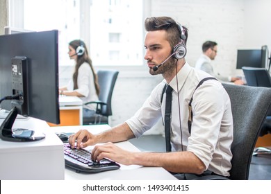 Handsome male call center worker talking with a client and using computer in office