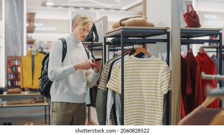 Handsome Male Customer Shopping In Clothing Store, Using Smartphone, Browsing Online, Comparing On Internet, Choosing Stylish Clothes. Fashionable Shop, Colorful Brands, Sustainable Designs