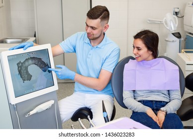 Handsome male dentist shows digital model of female patient's teeth made by 3d scanner.
