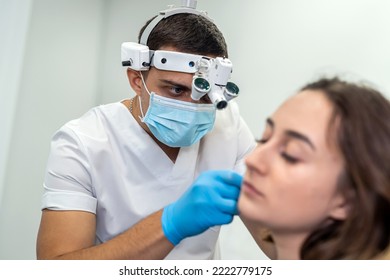 Handsome Male ENT In A Mask With A Lamp Makes An Examination Of A Girl Patient. Medicine. Examination Of The Diseased Ear