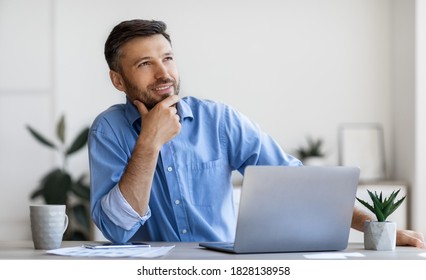 Handsome Male Entrepreneur Sitting At Workplace With Thoughtful Face Expression, Having Inspiration, Pensive Businessman Thinking About Business Strategy, Touching Chin And Smiling, Free Space