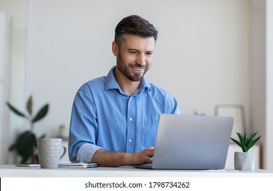 Handsome Male Entrepreneur Working On Laptop At Desk In Modern Office, Using Computer At Workplace, Typing On Keyboard, Copy Space