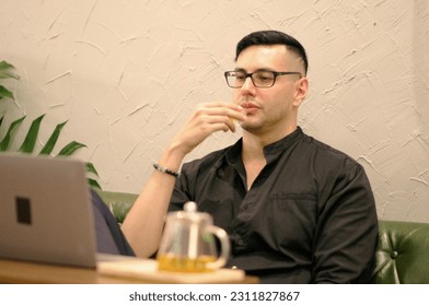 Handsome male freelancer enjoys working on laptop and thinking of new ideas while drinking morning tea in cafe - Shutterstock ID 2311827867