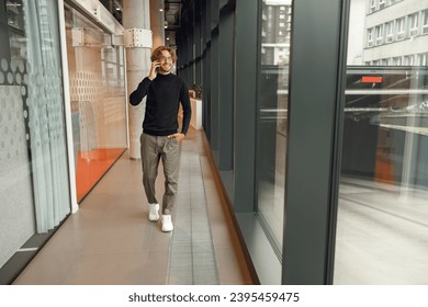 Handsome male freelancer in eyeglasses is talking phone standing in modern coworking space - Shutterstock ID 2395459475
