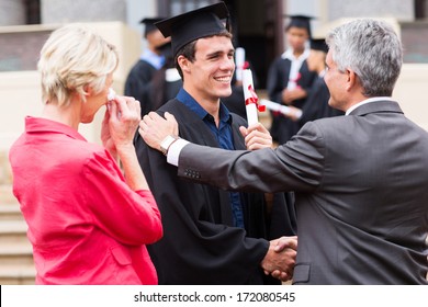handsome male graduate being congratulated by his father at graduation ceremony