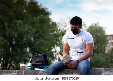 Handsome Male Latin Student Reading And Studying With A Mask Outdoor.