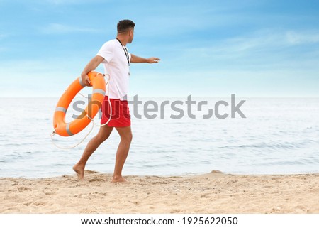Handsome male lifeguard with life buoy at sandy beach