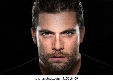 Handsome male model with masculine facial hair and intense eyes on isolated black background 