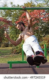 Handsome Male One Arm Pull Up Workout And Smat Phone Using. Street Workout Exercises. Extreme Sports.