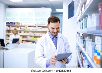 Handsome male pharmacist in white coat working in pharmacy store or drugstore. Checking medicines on his tablet computer. Healthcare and apothecary. - Powered by Shutterstock