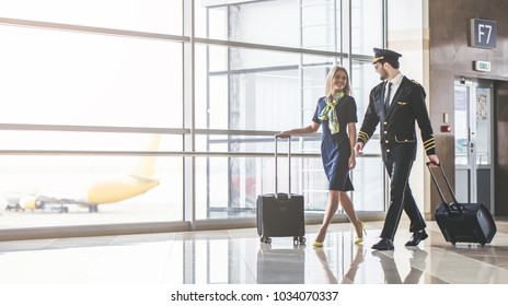 Красивый пилот мужского пола и привлекательная стюардесса ходят по терминалу аэропорта вместе.