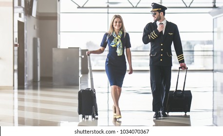 Handsome male pilot and attractive female flight attendant are walking in airport terminal together. - Shutterstock ID 1034070367