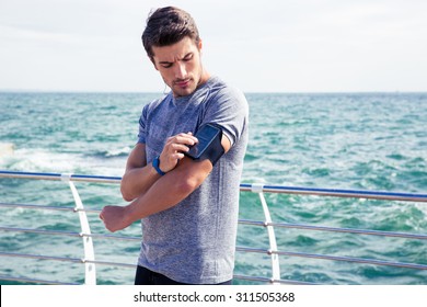 Handsome male runner listening to music adjusting settings on armband for smartphone outdoors - Powered by Shutterstock