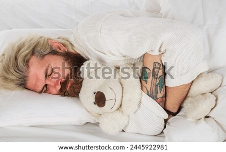 Handsome male sleeping with plush teddy bear relaxing in bed. Good night. Sleepy man in pajamas sleeping in bed at home with teddybear toy. Bearded man sleeping at bedroom and hugging soft teddy bear.