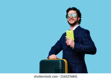 Handsome Male Traveler Tourist holds Passport and Suitcase on blue background. Pleased Bearded Man in Official Suit and Green Sunwear Traveling on Vacation Trip. Air Flight Business Class Journey
