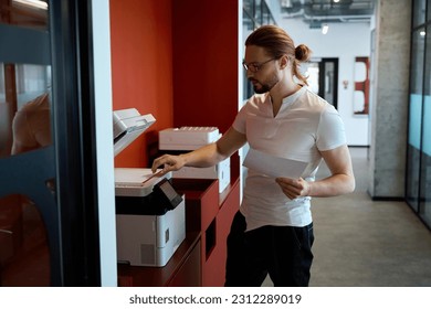 Handsome male worker using multifunction printer indoors