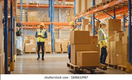 Handsome Male Worker Wearing Hard Hat Holding Digital Tablet Computer Walking Through Retail Warehouse Full Of Shelves With Goods. Professional People Working In Logistics And Distribution Cente