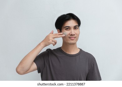 Handsome Man Applying Eye Cream Near Studio Portrait On Gray Background.