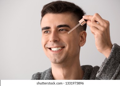 Handsome Man Applying Face Serum On Light Background