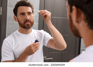 Handsome Man Applying Oil On Beard In Bathroom