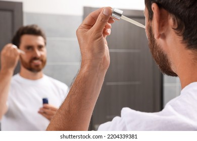 Handsome Man Applying Oil On Beard In Bathroom, Closeup