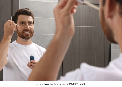 Handsome Man Applying Oil On Beard In Bathroom