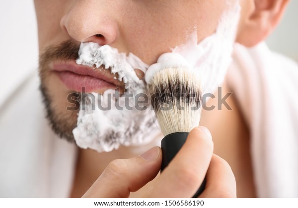 Handsome man applying shaving foam onto his face\
in bathroom, closeup