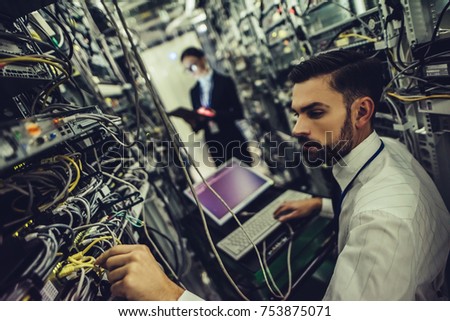Handsome man and attractive woman are working in data centre. IT engineer specialists in network server room. Running diagnostics and maintenance. Technicians examining servers.