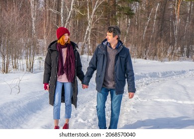 Handsome Man And Attractive Young Woman Walking Along Snowy Country Road In Sunny Day. Beautiful Look, Male And Female Fashion, Winter Outfit. Winter Holidays, Weekend At Countryside, Staycation