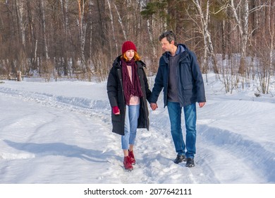 Handsome Man And Attractive Young Woman Walking Along Snowy Country Road In Sunny Day. Beautiful Look, Male And Female Fashion, Winter Outfit. Winter Holidays, Weekend At Countryside, Staycation