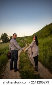 Handsome Man And Attractive Young Woman Walking Along Snowy Country Road In Sunny Day. Beautiful Look, Male And Female Fashion, Winter Outfit. Winter Holidays, Weekend At Countryside, Staycation.