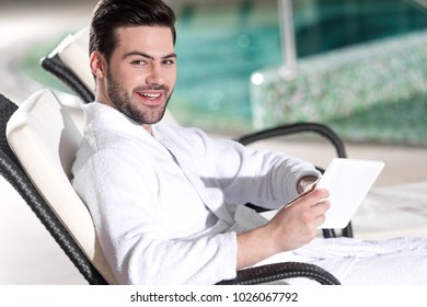 handsome man in bathrobe holding digital tablet and smiling at camera in spa center  - Powered by Shutterstock