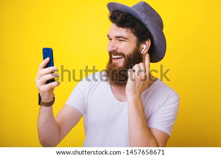 Handsome man with beard and hat, using mobie phone and airpods, isolated background 