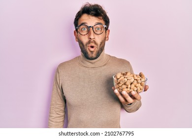 Handsome man with beard holding peanuts scared and amazed with open mouth for surprise, disbelief face 