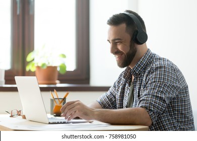 Handsome man with beard listening music in headphones and looking on screen of laptop. Young manager having a rest and playing in computer games or making video call on pc - Powered by Shutterstock